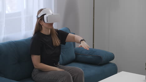 young-woman-is-using-head-mounted-display-for-viewing-interior-of-modern-house-sitting-on-couch-in-living-room-modern-technology